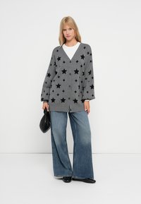 Grå cardigan med svarta stjärnmönster, V-ringning, knappstängning och överdimensionerade ärmar. Matchad med vida denimbyxor och en svart väska.
