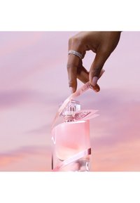 Klart glass parfymeflaske med en rosa væske, toppet med et diamantformet lokk. Dekorert med et lys rosa satengbånd og glitrende aksenter.