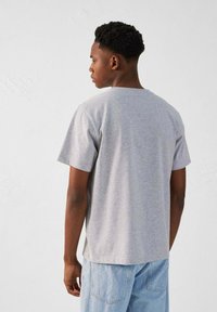 Camiseta de manga corta gris, hecha de algodón, con cuello redondo y corte relajado, mostrada desde la parte trasera sobre un fondo liso.