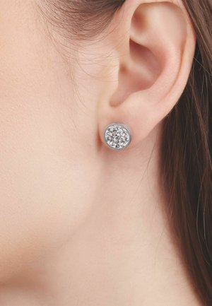 Zbliżenie na ucho noszące małą, okrągłą srebrną kolczyk z grupą przezroczystych kamieni szlachetnych.