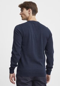 Temno modra pletena pulover iz mehkega materiala, z dolgimi rokavi, okroglim izrezom in rebrastimi manžete in robovi. Gladka tekstura z minimalističnim dizajnom.