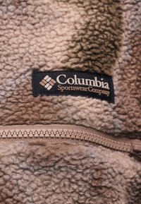Απαλό καφέ fleece ύφασμα της Columbia Sportswear Company με ορατή λεπτομέρεια φερμουάρ σε κοντινή λήψη.