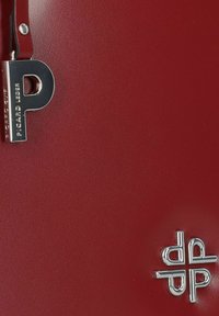 Rote Lederhandtasche mit glatter Textur und strukturiertem Design. Auffällige Beschläge sind ein silberner, monogrammierter Reißverschlussanhänger und ein Logo.