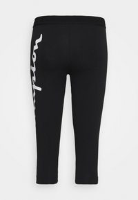 Leggings noirs courts avec ceinture élastique et grand texte blanc vertical sur la jambe gauche indiquant « Champion ».