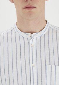 Camisa a rayas de color azul claro y blanco, hecha de tela texturizada con cuello alzado, que incluye botones y un bolsillo en el pecho.