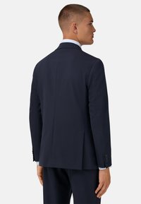 Granatowa marynarka z gładkiego materiału, dopasowany krój, pojedynczy rozcięcie z tyłu oraz mankiety na trzy guziki, zestawiona z jasnoniebieską koszulą. 