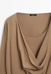 Beige stickad långärmad tröja med draperad polokrage, upphängd plant för att visa framsidan och etiketten med texten "Massimo Dutti."