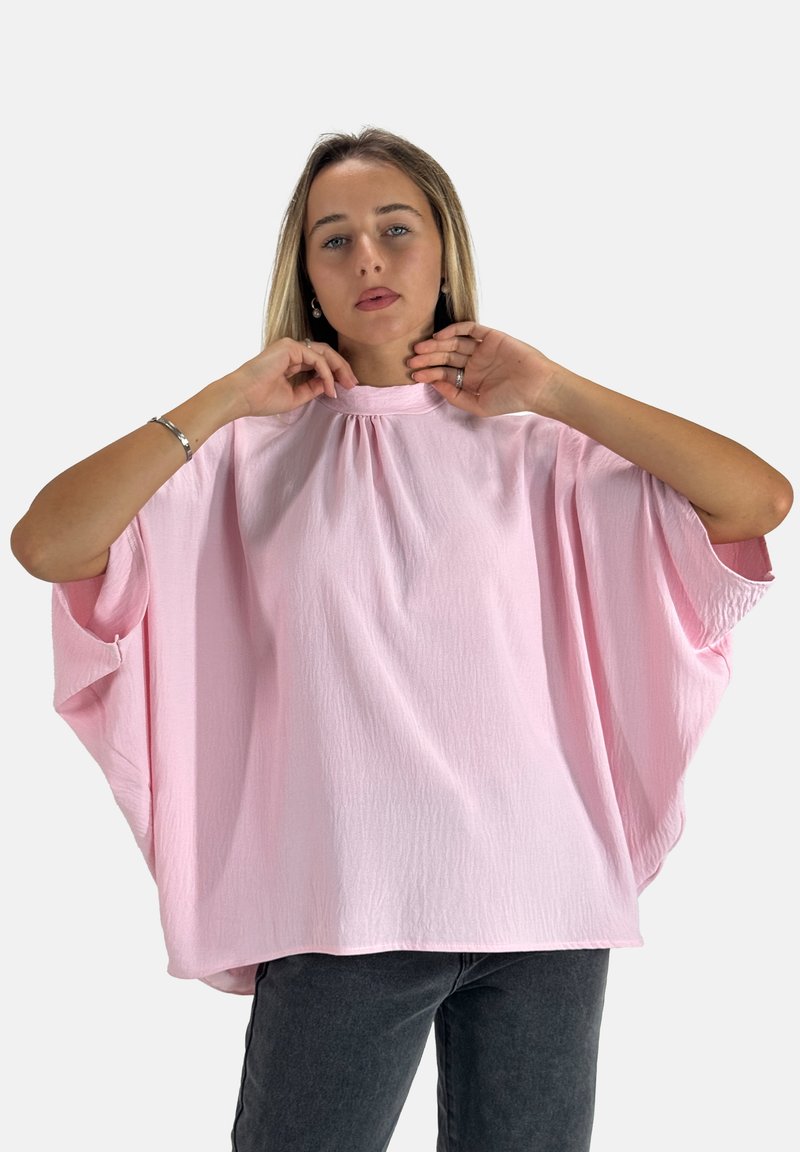 Rosa, locker sitzende Bluse mit hohem Ausschnitt und kurzen, weiten Ärmeln. Strukturierter Stoff mit subtilen Drapierungselementen. Kombiniert mit dunklen Jeans.