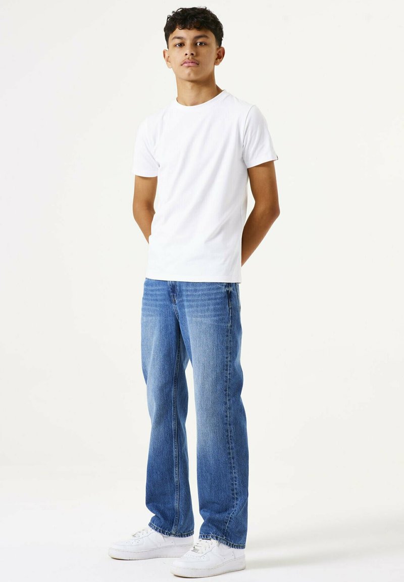 Camiseta blanca de manga corta combinada con jeans rectos de color azul claro, con textura suave y diseño básico, complementada con zapatillas blancas.