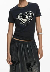 Černé tričko s krátkým rukávem a velkým grafickým motivem srdce se vzorem z novin a bílými detaily; tričko má přiléhavý krátký střih.