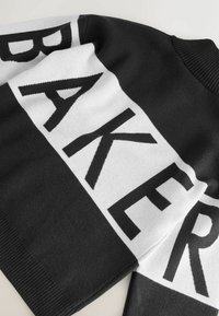 Suéter de punto con diseño en blanco y negro que presenta un atrevido estampado "BAKER". Textura suave, puños acanalados y cuello deportivo.