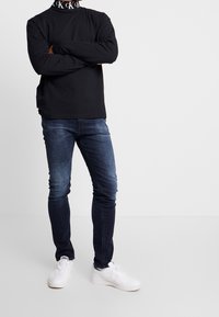 Svart långärmad t-shirt med logotypkrage, i kombination med mörkblå slim-fit jeans och vita sneakers. Enkelt design och avslappnad look.