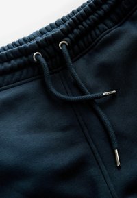 Pantalones de chándal azul marino con una cinturilla texturizada, cordón ajustable con puntas de metal plateado y tejido suave.