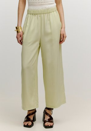 Helle grüne weite Hosen mit elastischem Taillenbund und seitlichen Taschen, aus einem glatten Stoff gefertigt. Kombiniert mit braunen Riemchen-Absatzsandalen.