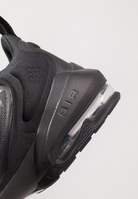 Zapatilla deportiva negra con un upper texturizado, que cuenta con una unidad de amortiguación de aire transparente en el talón y la palabra "AIR" grabada en el lateral.