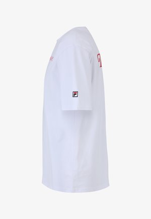 Biała koszulka z krótkim rękawem z czerwoną haftowaną aplikacją z przodu i małą naszywką w czerni, czerwieni i bieli na lewym rękawie.