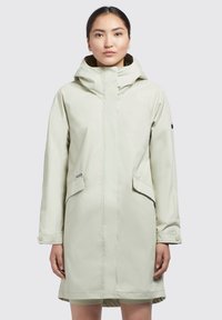 Parka impermeabil de culoare verde deschis, cu glugă, buzunare laterale și manșete cu capse. Prezintă o textură netedă și un design minimalist. Fundal simplu.
