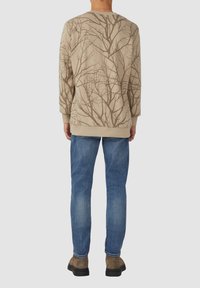 Felpa beige con motivo di rami, maniche lunghe, orlo a coste, abbinata a jeans blu e scarpe marroni. Design aderente.