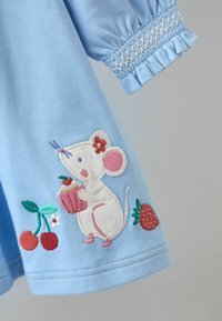 Zila kokvilnas kleita ar baltu izšūtu peli, kas tur kūciņu, kopā ar sarkaniem zemenēm un ķiršiem, un smockotiem pūkainiem piedurkņu galiem.