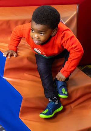 Blaue und grüne Schuhe mit einem Löwendesign, kombiniert mit einem roten Pullover und einer dunklen Jeans, beim Klettern auf einer bunten Oberfläche.