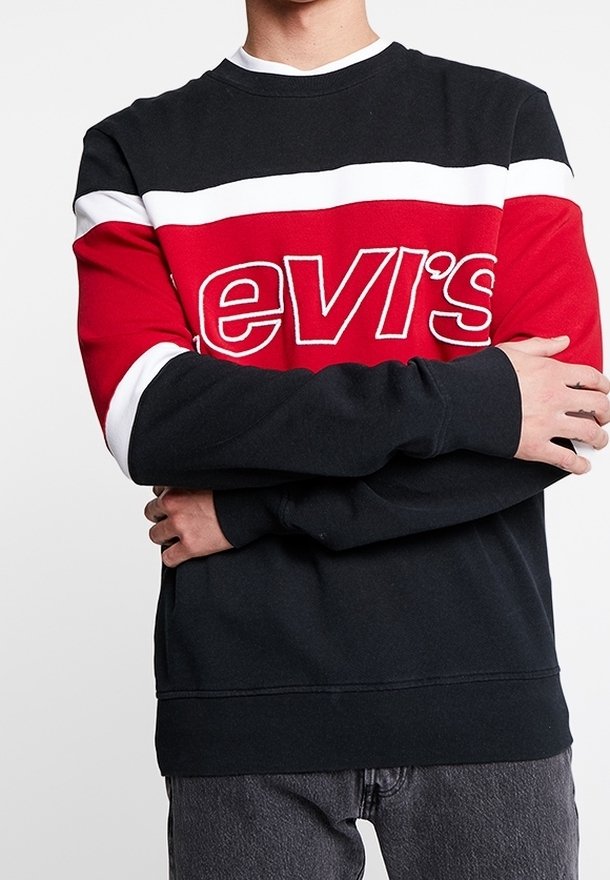Personne portant un sweat-shirt à blocs de couleurs avec des rayures noires, blanches et rouges ainsi qu’un grand texte blanc contouré « Levi's » sur la poitrine.