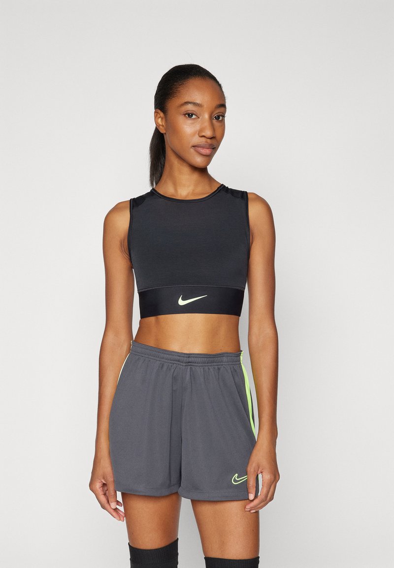 Top atletico corto nero con logo Nike neon, abbinato a pantaloni grigi con strisce laterali neon e vita elastica.