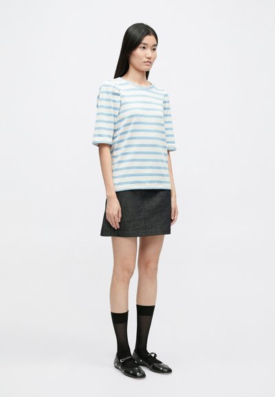 Ανοιχτού μπλε και άσπρη ριγέ βαμβακερή μπλούζα με κοντό μανίκι, συνδυασμένη με σκούρα τζιν μίνι φούστα, μαύρες κάλτσες και επίπεδα παπούτσια.