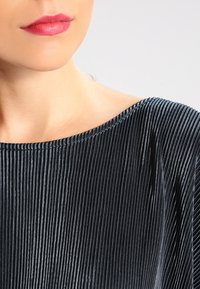 Tessuto plissettato nero con una superficie liscia, caratterizzato da un ampio scollo e linee orizzontali, mostrato su uno sfondo neutro.