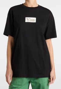 Sort bomulds t-shirt med et hvidt rektangulært Vans-logo i en stiliseret skrift, løst fit med korte ærmer og rund halsudskæring.