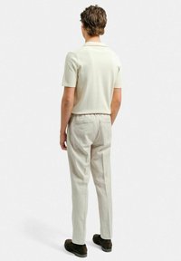 Ljusbeige kortärmad polo skjorta i kombination med ljusgrå byxor. Avslappnad passform, stickad textur och elastisk midja på byxorna. Bruna skor.