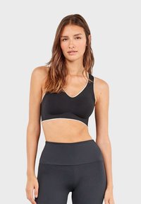 Zwarte sport-bh met een V-hals, witte rand langs de randen en een gladde stof. Draagt met zwarte high-waisted leggings.