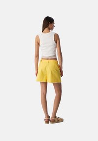 Geel denimshorts met rafelige onderkant, vijf zakken en een bijpassende riem. Het topje is een wit geribbeld hemd met een gaas inzet.