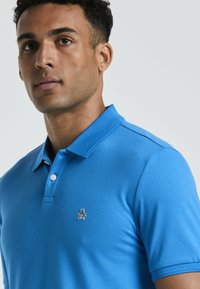 Blauwe polo van gestructureerde katoen, met een col met twee knopen, korte mouwen en een klein zwart-wit logo op de linkerborst.