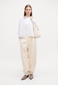 Biely a béžový outfit s pruhovanou skrátenou bundou, jednoduchým topom a širokými nohavicami. Doplnky zahŕňajú svetlú tašku a neutrálné topánky.