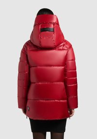 Rode pufferjack met een hoge kraag en een oversized capuchon. Bevat gequiltte secties, matte afwerking en een logo-detail op de achterkant.