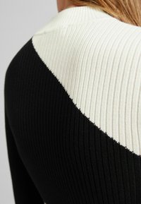 Le pull en tricot noir et crème à côtes présente un design diagonal. Le tissu texturé met en valeur les couleurs contrastées.