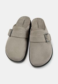 Scarpe slip-on in suede grigio con un accento di fibbia metallica, punta tonda e suola in gomma nera. Texture liscia con dettagli di cucitura minimi.