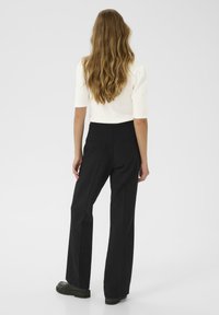 Top bianco a maniche corte abbinato a pantaloni neri a vita alta. I pantaloni hanno un design su misura con tasche posteriori e gamba dritta.