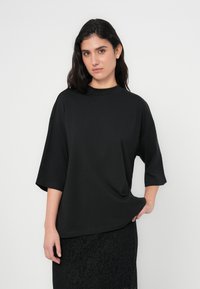 T-shirt preta oversized feita de tecido macio, com gola alta e mangas curtas, combinada com uma saia preta de renda.