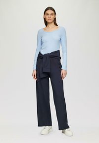 Helles blaues Langarmoberteil mit weitem Ausschnitt, kombiniert mit navyblauen, weit geschnittenen Hosen, die an der Taille gebunden sind. Weiße, klobige Sneaker runden den Look ab.