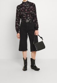 Musta kukkakuosiset pitkät hihaiset puserot, korkeavyötäröiset mustat culottes-housut, mustat cowboy-kengät ja teksturoitu musta käsilaukku, jossa on solmittu kahva.