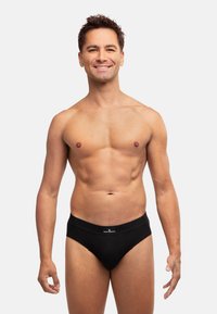 Schwarze Baumwollslips mit glatter Textur und elastischem Taillenbund, präsentiert an einem Modell mit muskulösem Körperbau.