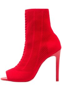 Botte courte rouge en tricot à bout ouvert avec un haut talon aiguille et des panneaux en tissu texturé et respirant.