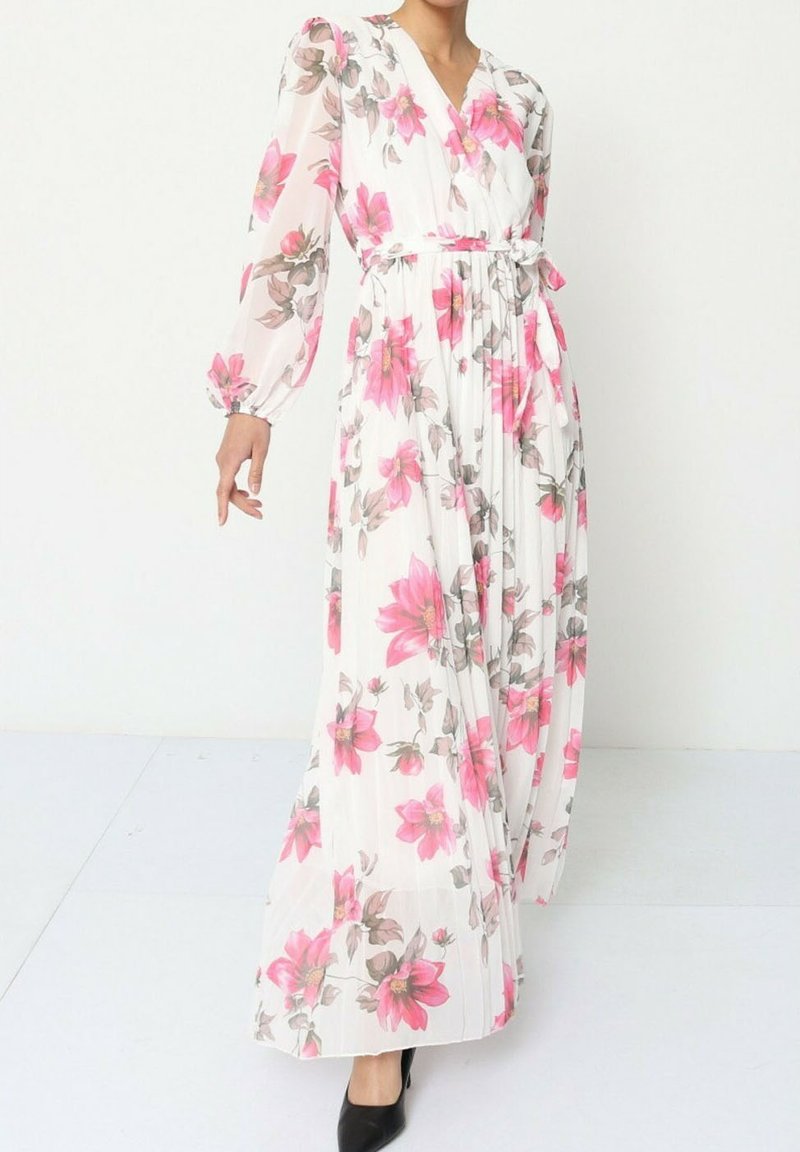 Robe maxi florale en tissu blanc avec des motifs de fleurs roses et grises, manches longues, col en V et une ceinture à nouer, accompagnée de talons noirs.