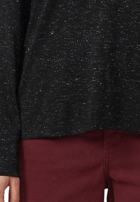 Zwarte lange mouwen top met een losse pasvorm, met een textuurpatroon en subtiele glitters; gecombineerd met bordeauxrode broek.