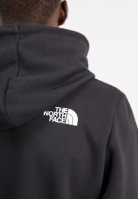 Zwarte hoodie met een zachte textuur, voorzien van een wit logo van "The North Face" op de rug boven de halslijn. Casual ontwerp.