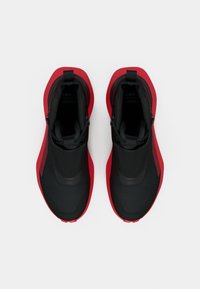 Sportschuhe mit einem schwarzen Textil-Obermaterial und roten Akzenten, einer stromlinienförmigen Form und einer strukturierten Sohle für besseren Halt. Ohne Schnürsenkel, im Slip-On-Design.
