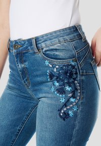 Spijkerbroeken met ingewikkeld blauwe bloemenborduursel op de voorkant, met een klassieke slim fit en een vervaagde lichtblauwe wassing.