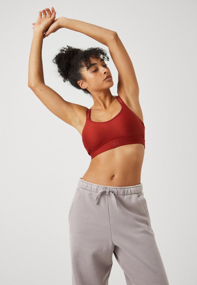 Roter Sport-BH mit glatter Textur und breiten Trägern, die Akzente des Logos aufweisen, kombiniert mit hellgrauen Sweatpants mit Kordelzugbund.