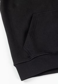 Mustast dressipluusist varrukas, millel on soonikkoes varrukasõlm ja nurga all olev esitasku, valgel taustal.